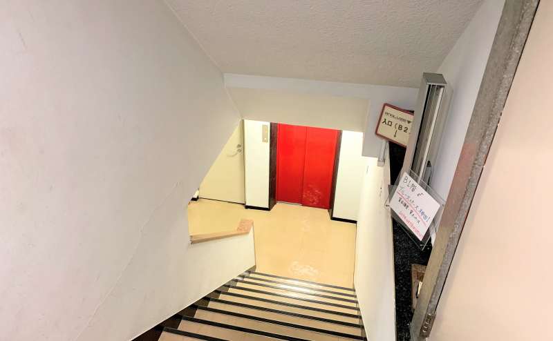 １F階段となります。赤いエレベーターの隣が当スペースのドアとなります。